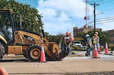 City of Bryan employees dressed in safety gear performing construction on a roadway with orange traffic cones marking the area.