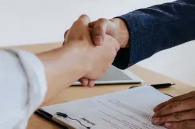 interviewer shaking hands with job applicant over a desk.