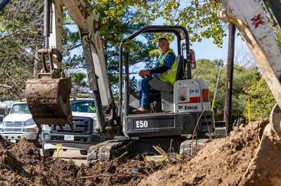 worker operating machinery to dig and uncover water pipes