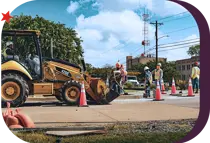 City of Bryan employees dressed in safety gear performing construction on a roadway with orange traffic cones marking the area