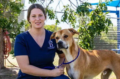Bryan Animal Center staff member kneeling beside a dog