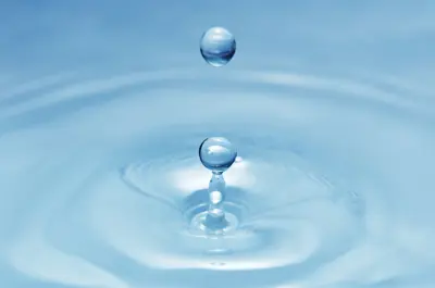 water droplet rippling in a pool of clean clear blue water