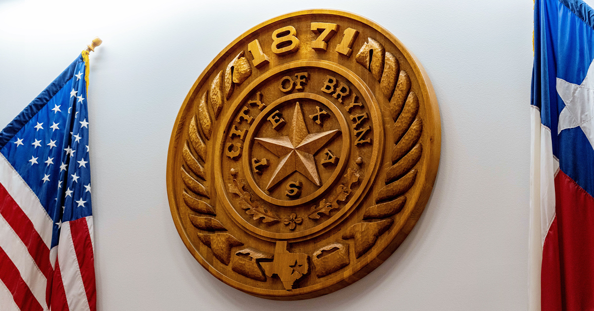 wooden plaque of the City of Bryan seal resting between two flags.